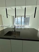 Modern kitchen island featuring a solid-surface countertop, integrated stainless steel undermount sink, gooseneck faucet, and four cylindrical pendant lights