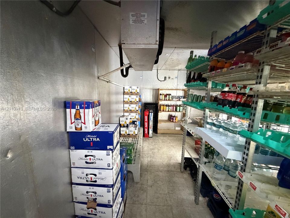 Walk-in refrigeration unit featuring insulated metal wall panels, ceiling-mounted refrigeration system, and industrial-grade shelving units