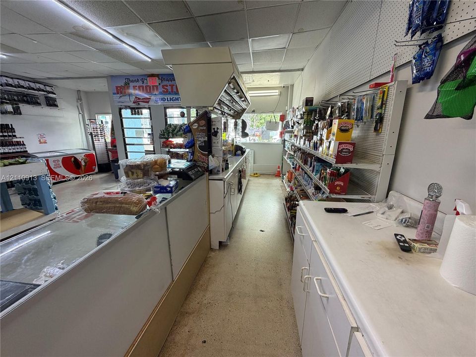 Retail space featuring commercial-grade vinyl flooring, a drop ceiling with fluorescent lighting, fixed perimeter shelving, a stainless steel exhaust hood, and a built-in service counter