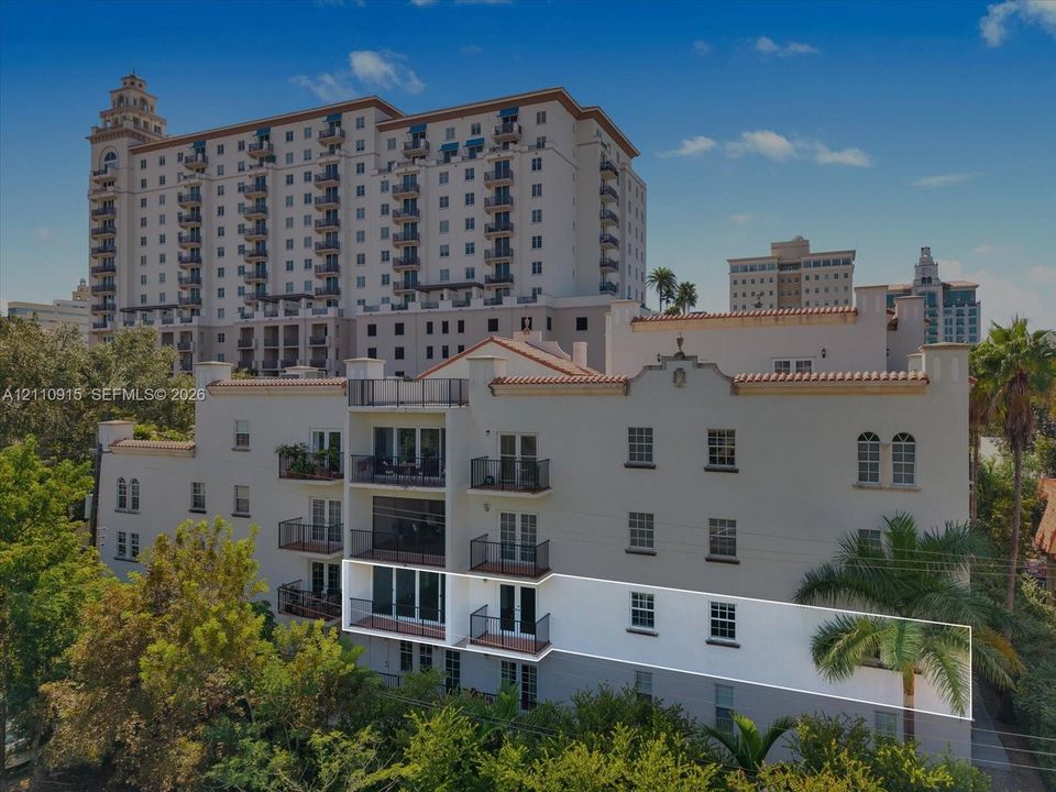 Multi-story stucco exterior featuring arched windows, tile roof accents, and metal balcony railings