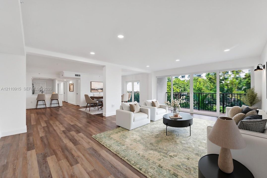 Open-concept interior featuring wood-finish flooring, recessed lighting, expansive sliding glass doors, and a private balcony with metal railing