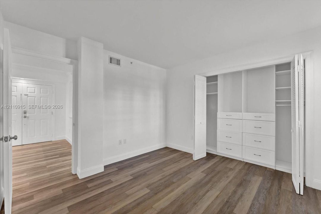 Room featuring wood-finish flooring, built-in closet system with integrated shelving and drawers, and paneled interior doors