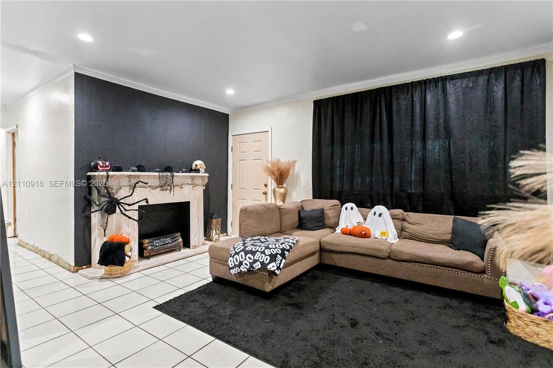 Living area featuring neutral tile flooring, a fireplace with a decorative stone-finish mantle, recessed ceiling lighting, and a prominent black accent wall