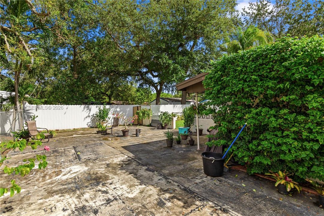Fenced backyard featuring a concrete patio, a covered structure, and mature trees