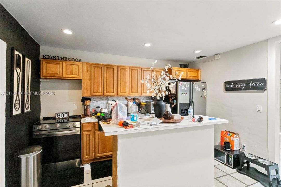 Kitchen featuring light-finish cabinetry, a breakfast bar with a solid-surface countertop, recessed ceiling lighting, and tile flooring