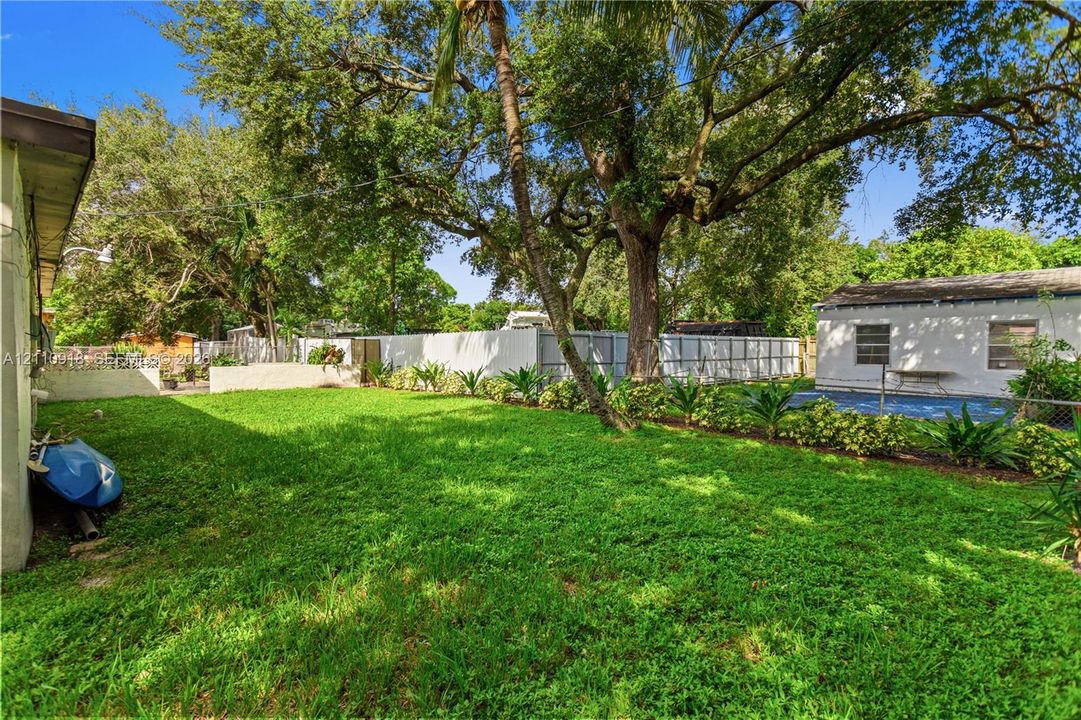 Expansive backyard featuring a manicured lawn, mature trees, privacy fencing, and a swimming pool