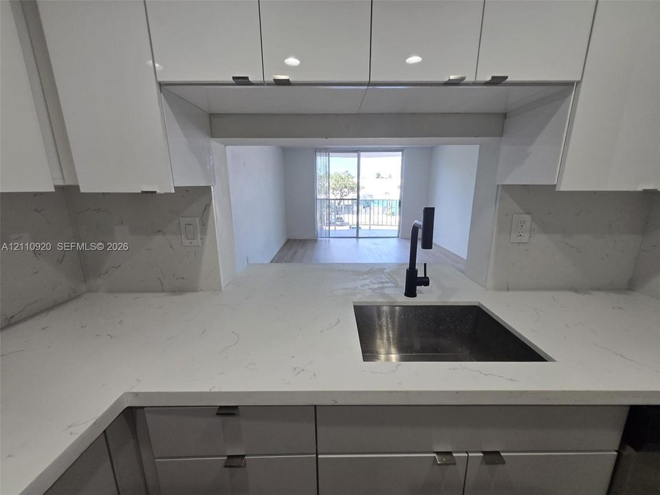 Kitchen featuring high-gloss white cabinetry, stone-surface countertops, matching backsplash, and a matte black faucet with an integrated sink