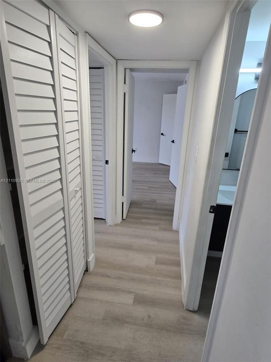 Hallway featuring wood-finish flooring, white louvered closet doors, and flush-mount overhead lighting