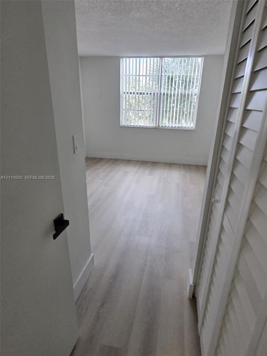 Interior space featuring wood-finish flooring, white louvered closet doors, and a large window with vertical blinds
