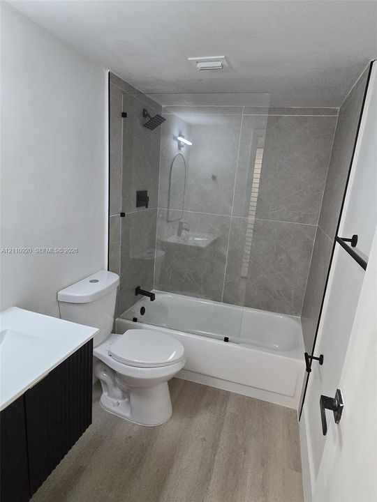 Full bathroom featuring a tub-shower combination with floor-to-ceiling large-format tile surround and a glass panel
