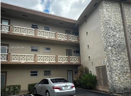 Three-story building exterior featuring textured stone masonry facade, multi-level balconies with geometric lattice railings, and exterior-access entry doors