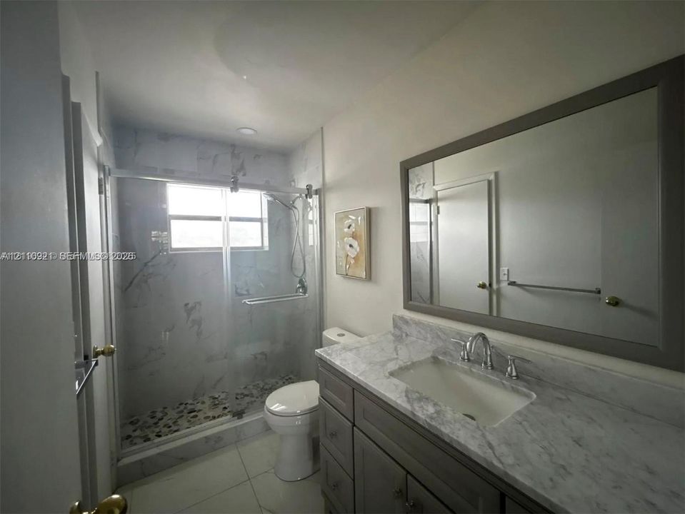 Bathroom featuring a stone-surface vanity with an integrated basin, a large framed wall mirror, a glass-enclosed shower with tiled walls, and stone-tile flooring
