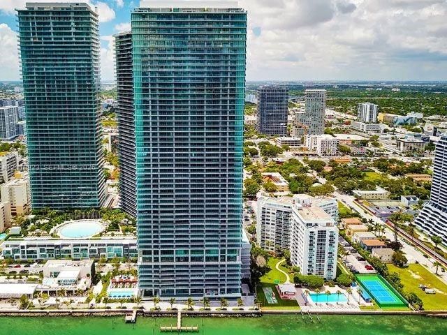 High-rise glass facade residential tower featuring wrap-around balconies, deep-water dockage, multiple swimming pools, and a tennis court