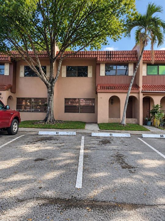 Two-story stucco exterior featuring a red tile roof, arched entryway, and dedicated assigned parking spaces