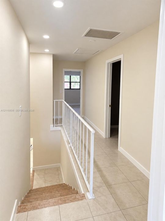 Hallway featuring large-format ceramic tile flooring, neutral wall tones, recessed lighting, and a white metal staircase railing