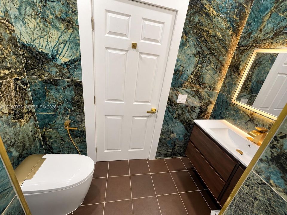 Floor-to-ceiling stone-finish wall tile, floating wood-finish vanity with integrated sink, brass-tone hardware, wall-mounted faucet, and square-tile flooring