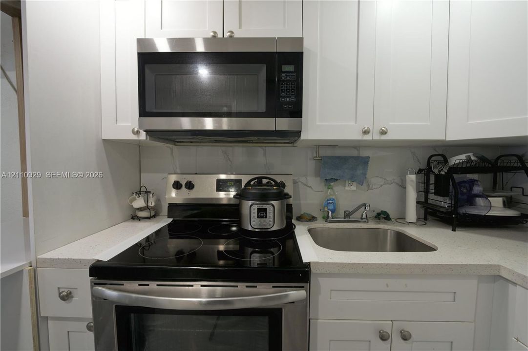 Kitchen featuring white shaker-style cabinetry, solid-surface countertops, a stainless steel electric range, an integrated over-the-range microwave, and a stainless steel undermount sink