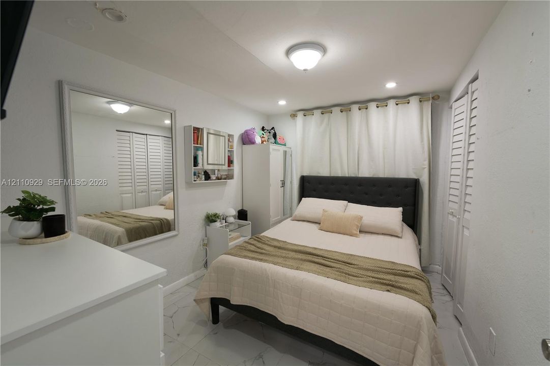 Large wall-mounted mirror, white tile flooring, louvered closet doors, and recessed lighting