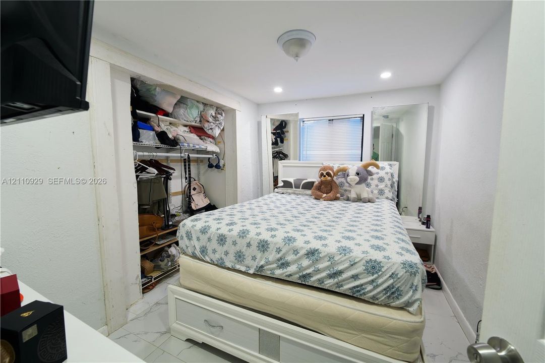 Bedroom featuring white marble-finish tile flooring, recessed lighting, and a built-in recessed closet