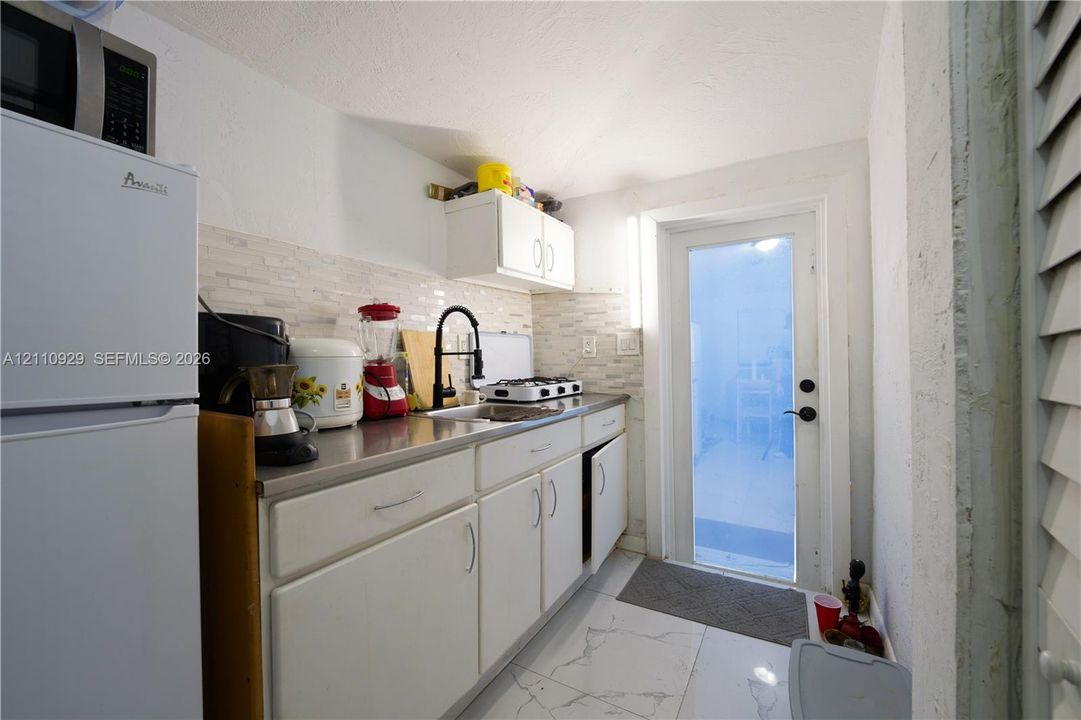 Kitchenette featuring white cabinetry, metallic countertop, stone-tiled backsplash, high-arc faucet, and large-format porcelain tile flooring