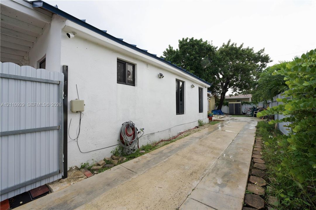 Stucco exterior finish with inset windows, white metal side gate, and concrete paved pathway