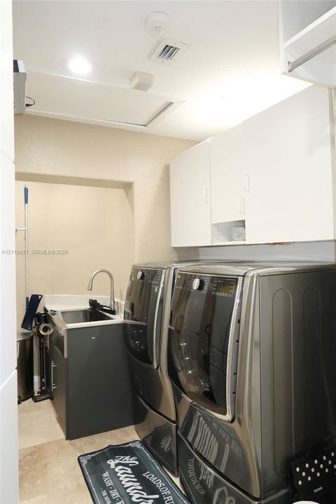 Utility space featuring white overhead cabinetry, stone-finish countertops, an under-mount sink with a high-arch faucet, and neutral tile flooring