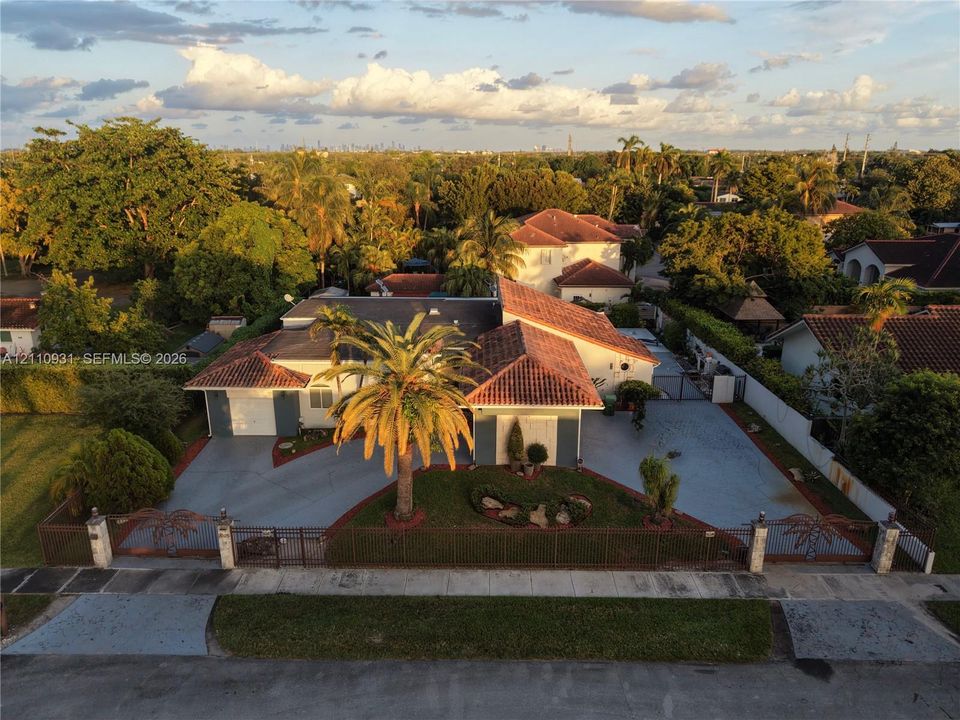 Single-story residence featuring a terracotta-tiled roof, an expansive paved driveway, and decorative metal perimeter fencing