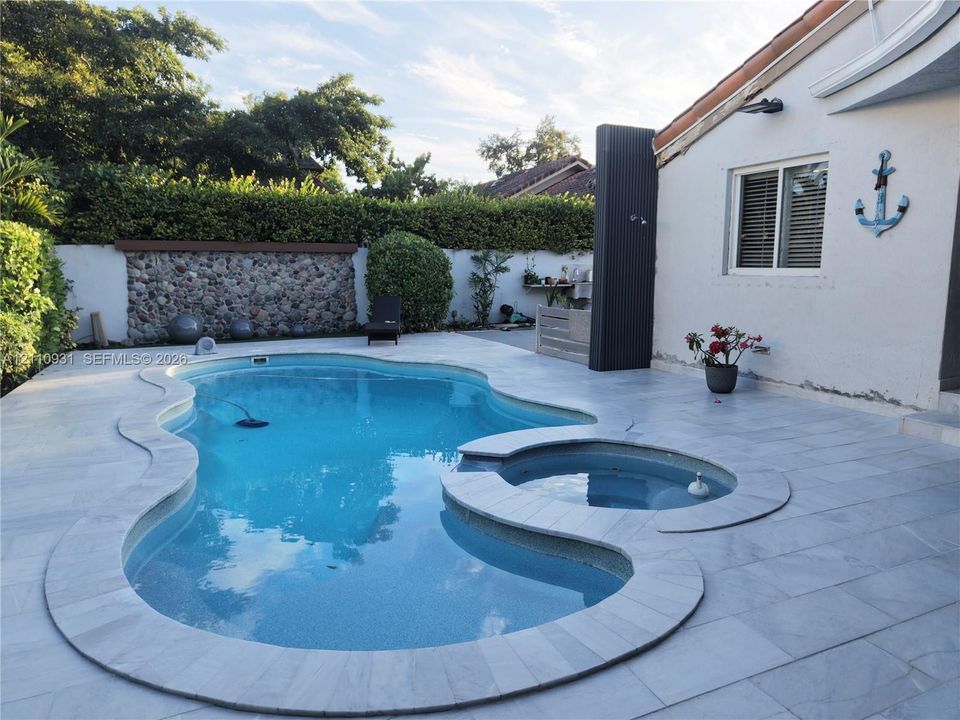 Inground swimming pool with attached circular spa, surrounded by stone-tile decking and bordered by a decorative stone-accent wall