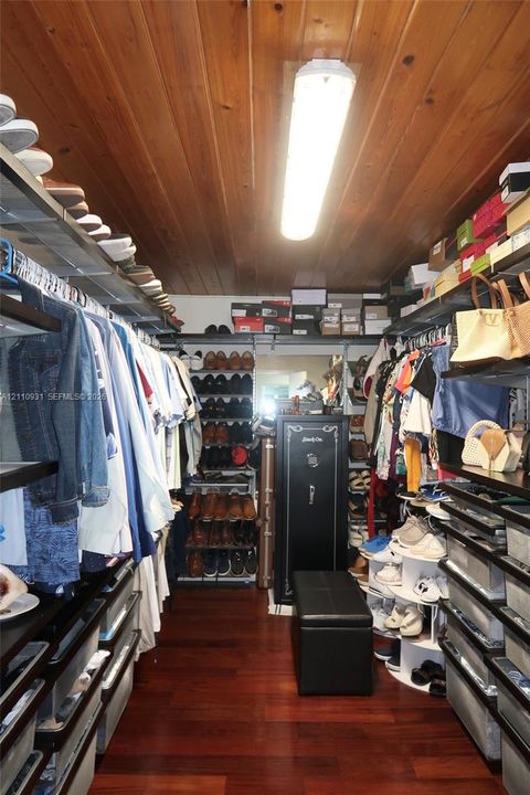 Walk-in storage space featuring wood-finish flooring, paneled wood ceiling, tiered shelving, and built-in linear ceiling lighting
