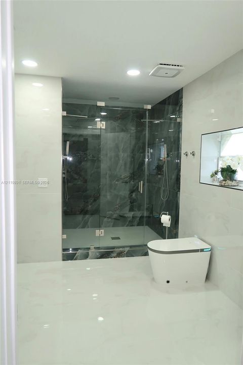 Walk-in glass-enclosed shower with dark stone-patterned tile, white floor-to-ceiling wall tile, recessed lighting, and a modern low-profile toilet