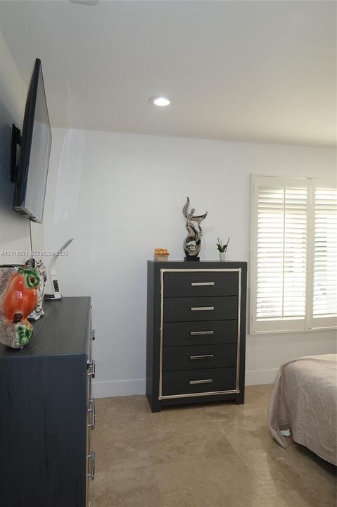 Neutral-toned stone flooring, recessed ceiling lighting, and plantation-style window shutters