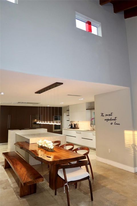 Modern kitchen featuring flat-panel cabinetry, a central island with a stone-surface waterfall edge, high ceilings with exposed wood beams, clerestory windows, and recessed lighting