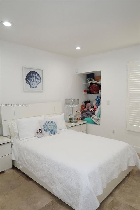 Neutral-toned tile flooring, built-in recessed shelving, integrated ceiling lighting, and plantation-style window shutters