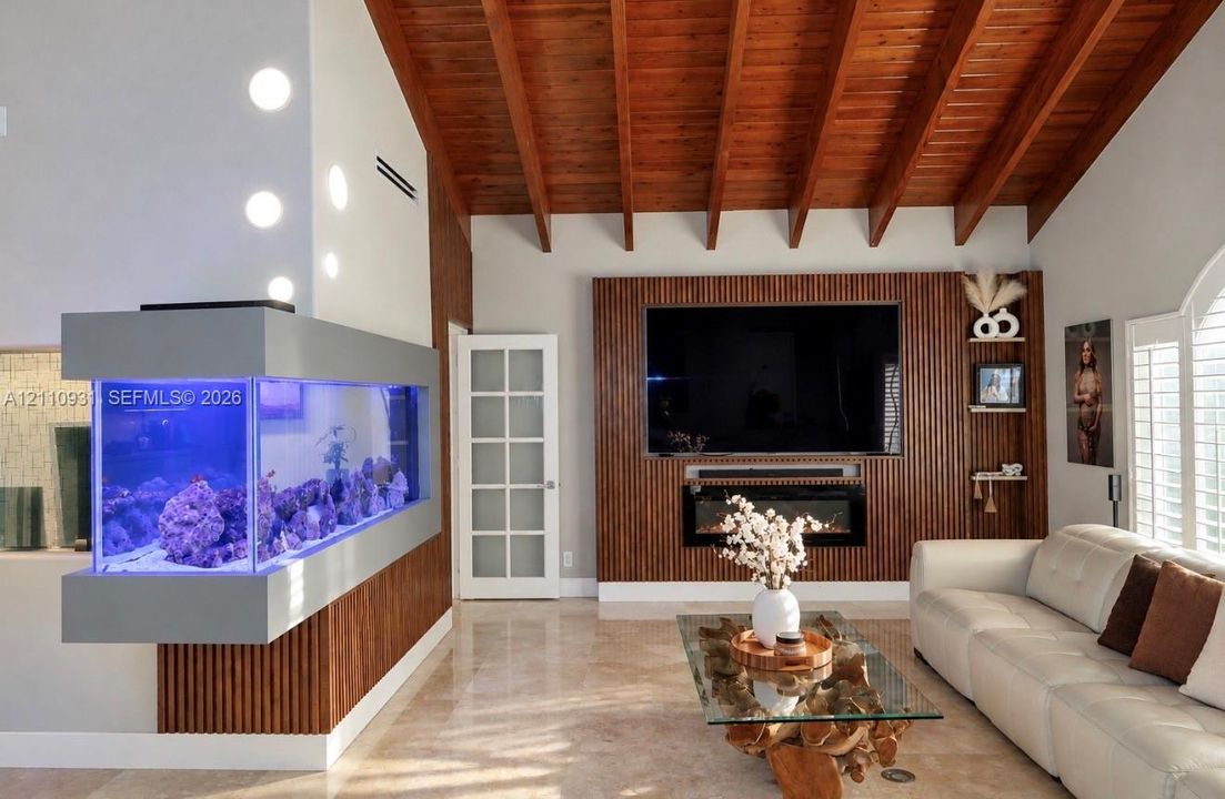 Vaulted wood-plank ceiling with exposed rafters, custom floor-to-ceiling slatted wood wall paneling, built-in electric fireplace, wall-mounted aquarium, and polished stone flooring