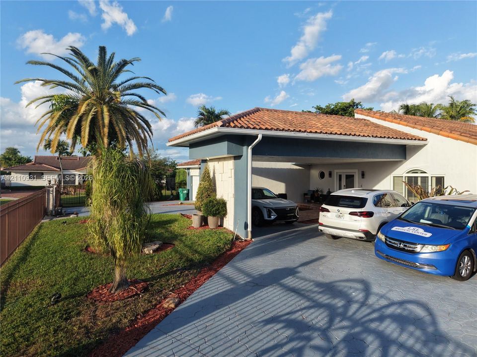 Single-story exterior featuring a clay tile roof, attached covered carport, textured stucco facade, and a stamped concrete driveway
