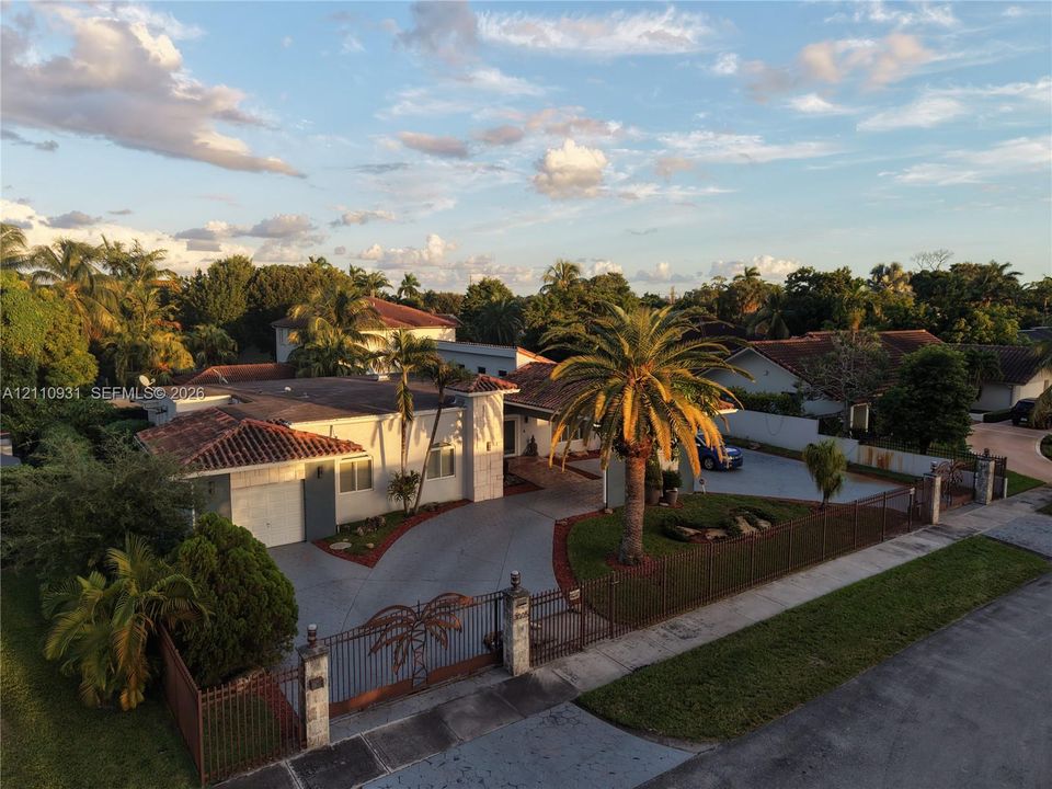 Single-story residence featuring a tile roof, gated concrete driveway, metal perimeter fencing, and mature palm landscaping