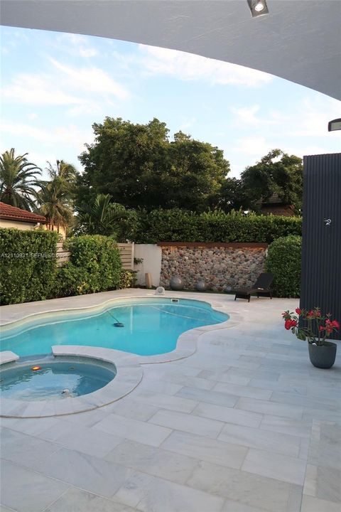 Free-form swimming pool with integrated spa, stone-accented perimeter wall, and light-toned paved decking