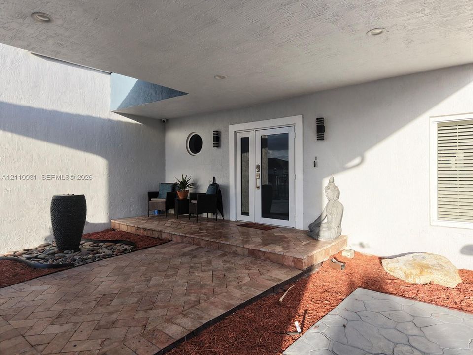 Covered entryway featuring herringbone-pattern tile flooring, double-door entry, recessed lighting, and a circular accent window