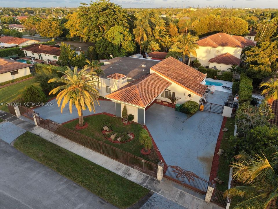 Aerial perspective of a single-story residence featuring a terracotta-tiled roof, an integrated carport, a paved driveway, and an in-ground swimming pool