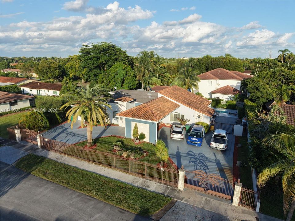 Single-story residence featuring a clay tile roof, expansive paved driveway, decorative metal perimeter fencing, and mature landscaping