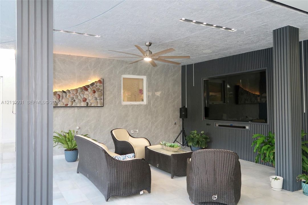Covered patio featuring large-format stone-finish wall tiling, vertical ribbed accent paneling, recessed ceiling lighting, and a ceiling fan