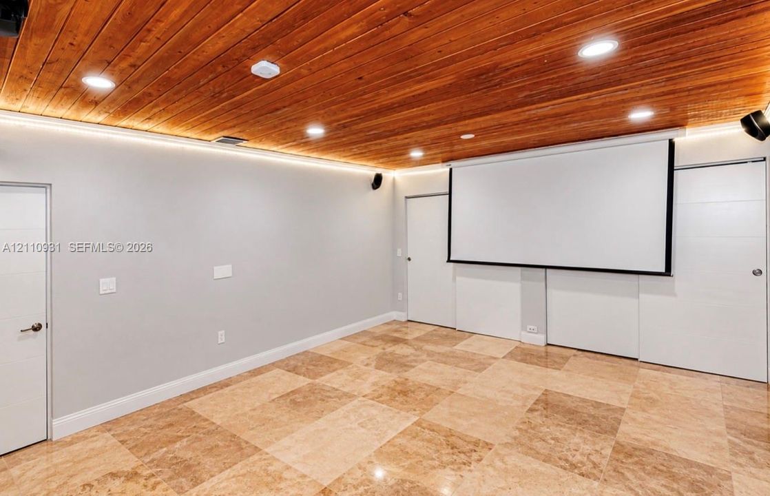 Tongue-and-groove wood plank ceiling, recessed lighting, integrated perimeter accent lighting, wall-mounted projection screen, and polished stone flooring