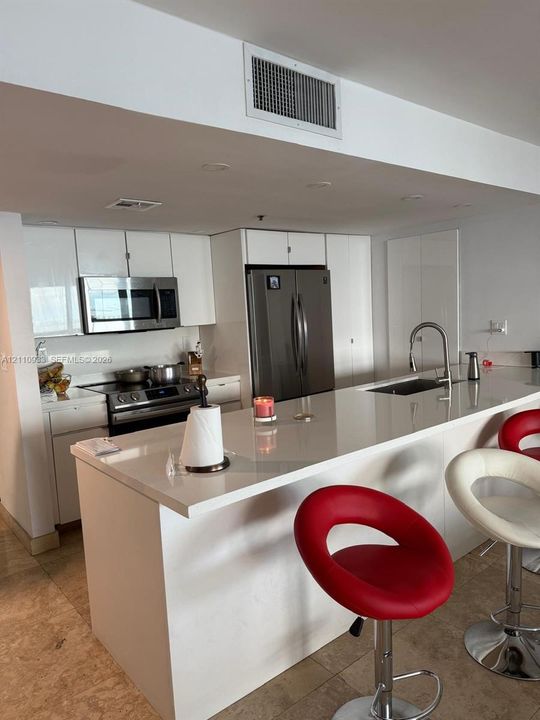 Kitchen featuring white cabinetry, solid-surface countertops, a center island with an integrated sink and gooseneck faucet, stainless steel appliances, and stone flooring