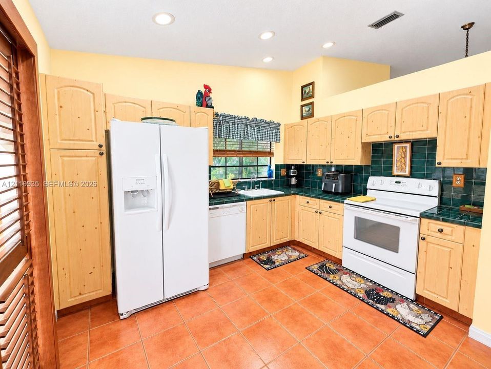 Kitchen featuring light wood-finish cabinetry, emerald green tile backsplash and countertops, ceramic tile flooring, and recessed lighting