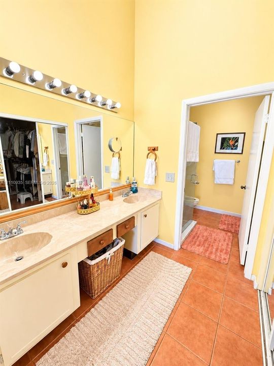 Dual-sink vanity with solid-surface countertop, full-width wall-mounted mirror, tiered vanity lighting, and ceramic tile flooring