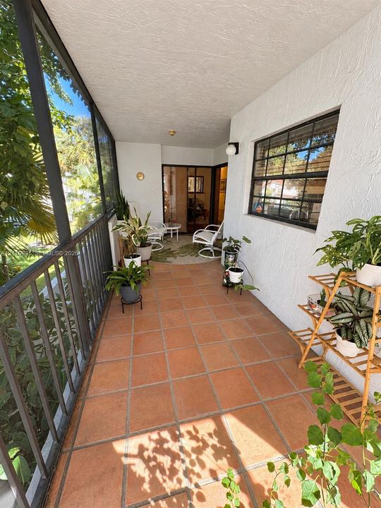Screened-in porch featuring terracotta tile flooring, textured stucco walls, and black-framed metal railings
