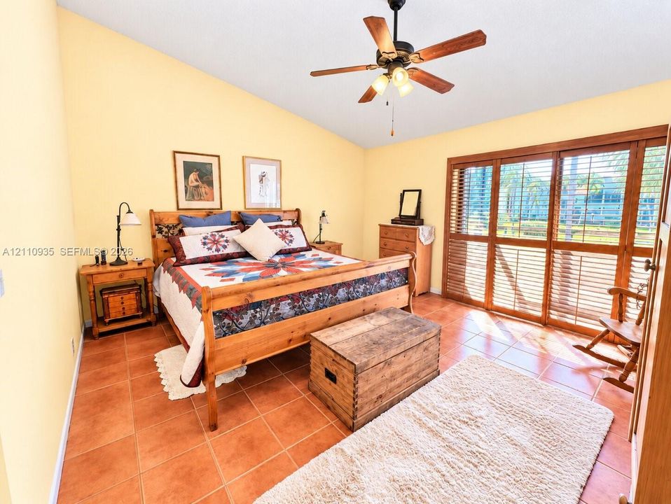 Vaulted ceilings, terra cotta tile flooring, and floor-to-ceiling wooden-frame sliding glass doors featuring integrated shutters and a central ceiling fan with multi-light fixture