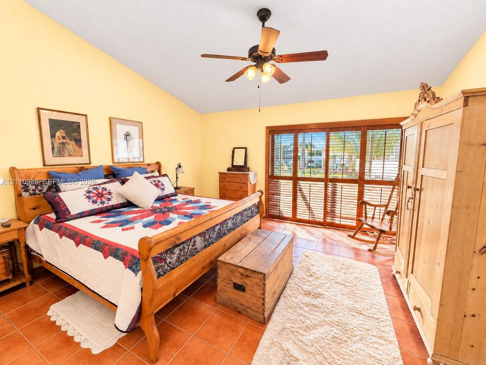 Vaulted ceiling, ceiling fan with integrated lighting, tile flooring, and floor-to-ceiling sliding glass doors with wood trim