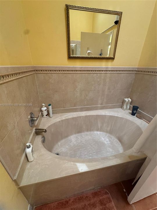 Oval soaking tub with a tiled surround, decorative chair rail tile accent, and wall-mounted metallic fixtures, complemented by a rectangular wall-mounted mirror