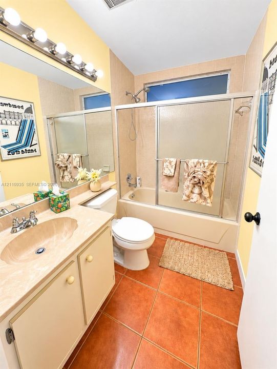 Bathroom featuring terracotta-style tile flooring, vanity with integrated sink, full-width wall mirror, and tub-shower combination with sliding glass doors